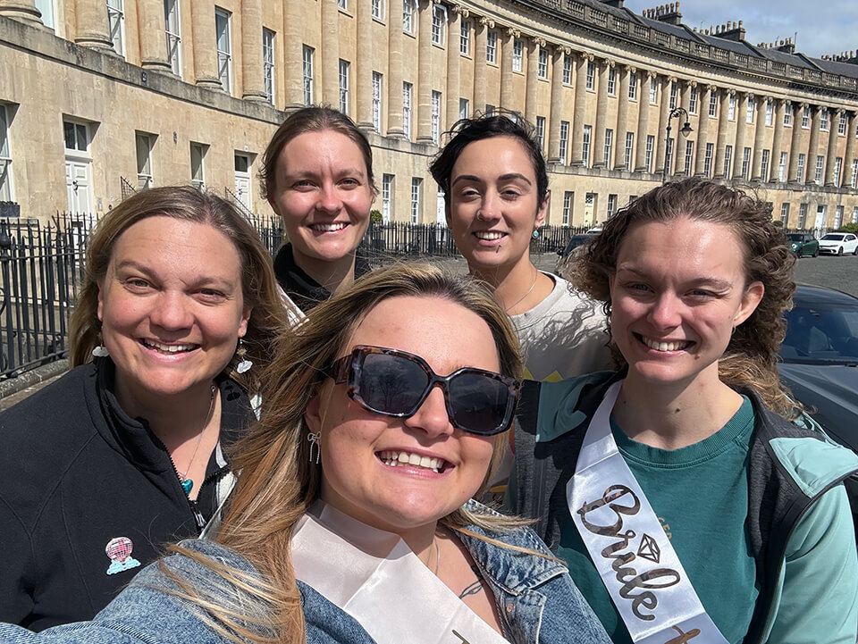 A group of women on a hen party taking a selfie, with bright sunshine and sashes reading &ldquo;Bride Tribe&rdquo; and &ldquo;Bride to Be&rdquo;.