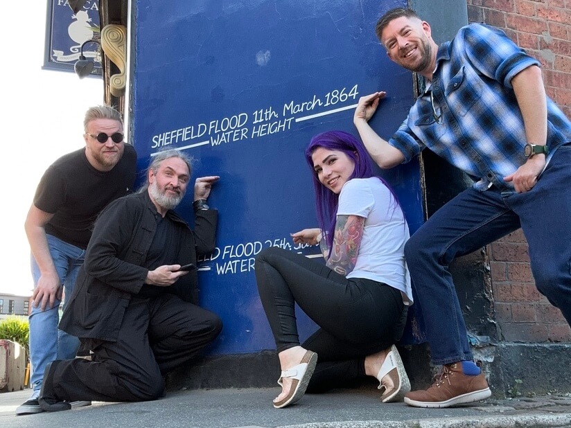 Four people posing by a flood sign while out on a treasure hunt as part of their work do.