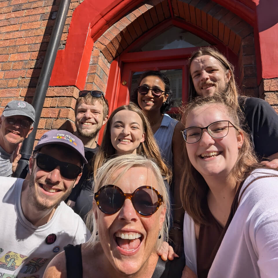 Happy friends posing for a group photo outside a red-brick building during a UK city treasure hunt tour.